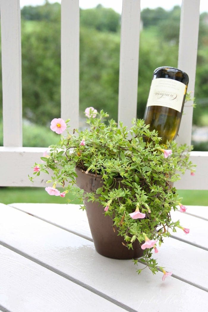 A vase of flowers on a white porch with a wine bottle inside. 