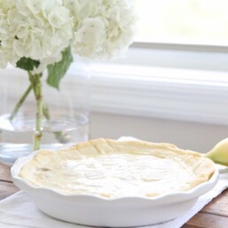 easy banana cream pie recipe in white pie dish with white flowers in vase in background