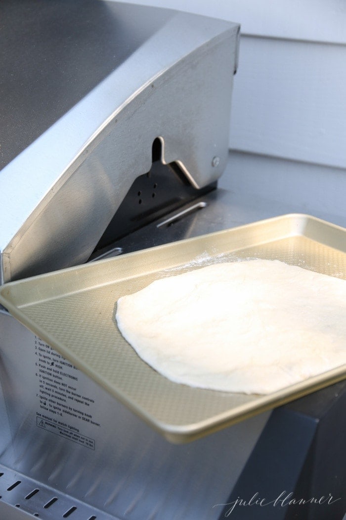 Pizza dough on a gold baking pan near a grill