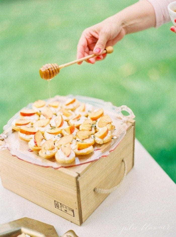 Peach Crostinis on a serving plate being drizzled with honey