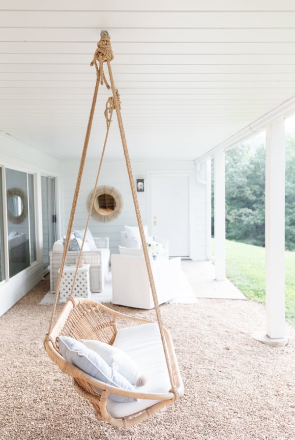 A wicker swing, ideal for outdoor living, is hanging from a porch.