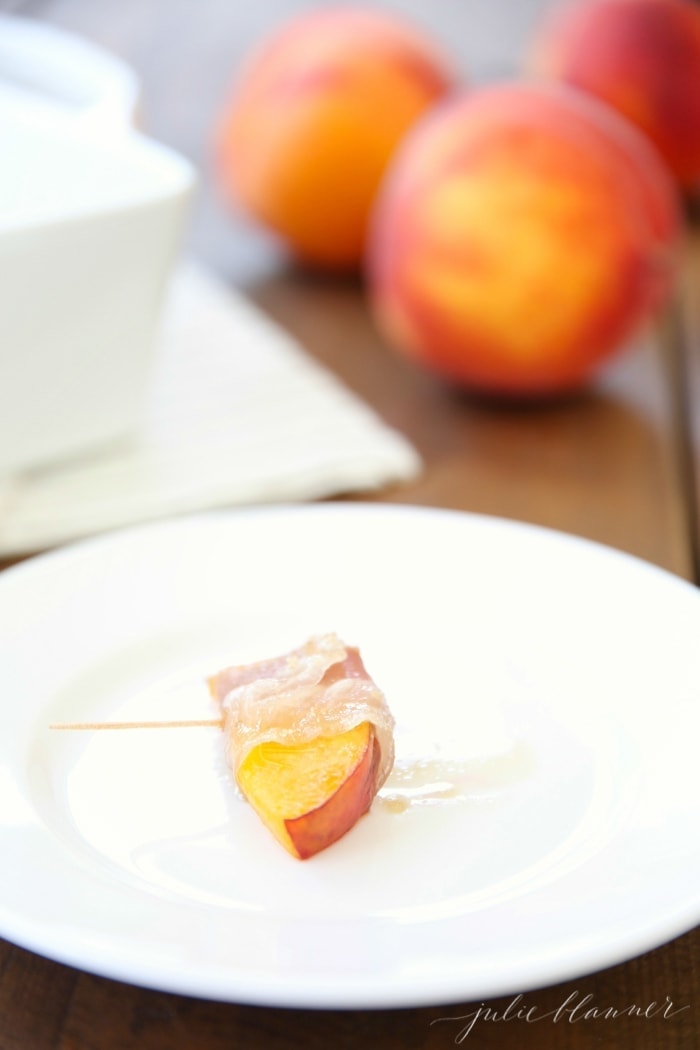 Prosciutto wrapped peach on a skewer on a white plate