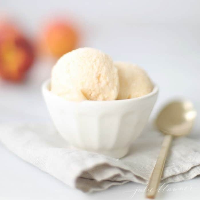 No churn homemade peach ice cream recipe in a white bowl placed on top of a linen kitchen towel.