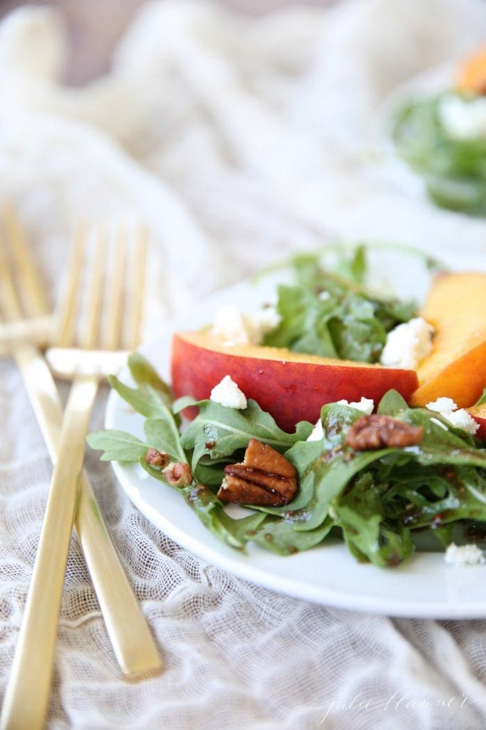 Peach salad with vinaigrette served on a white plate with a gold fork