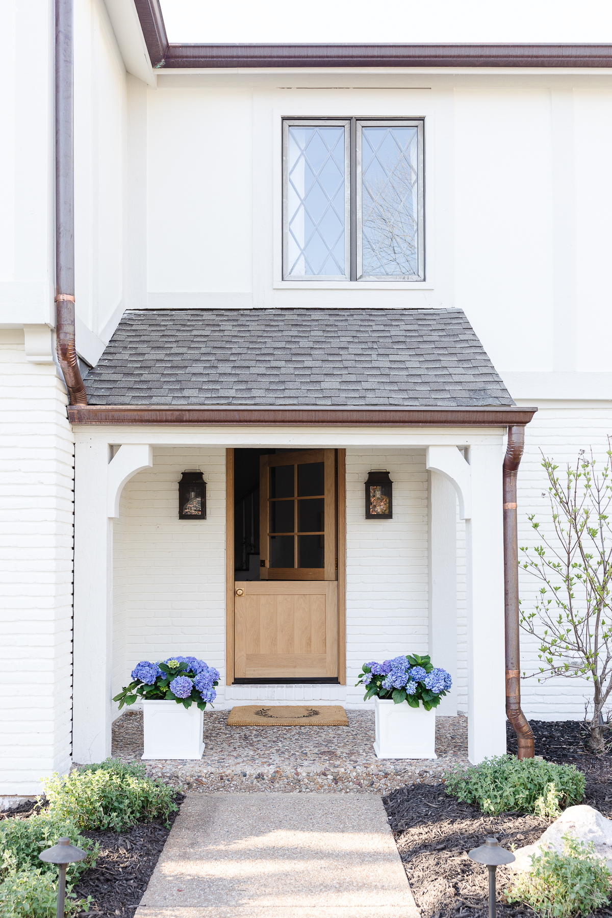 White front porch planters with blue hydrangea on a small covered front porch. 