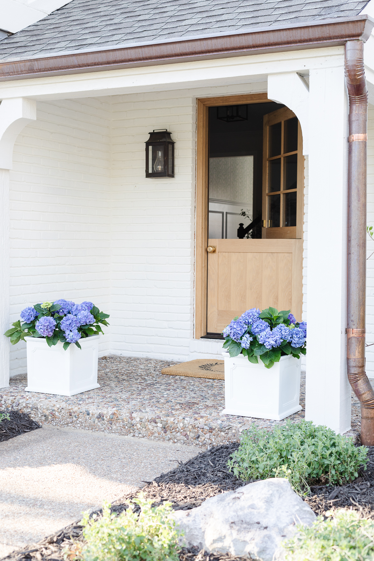 A white front porch planter with blue hydrangea on a small covered front porch.