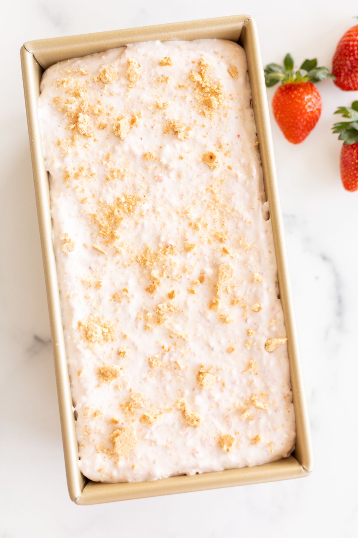 A gold loaf pan filled with creamy homemade strawberry cheesecake ice cream.