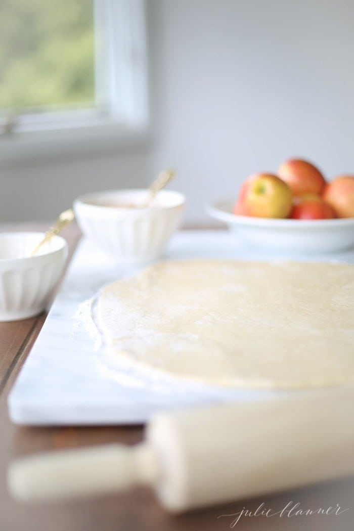 Dough rolled out on a work surface, a bowl of apples in the background