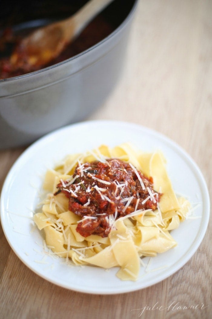 braised beef ragu on bed of pappardelle on white plate next to dutch oven