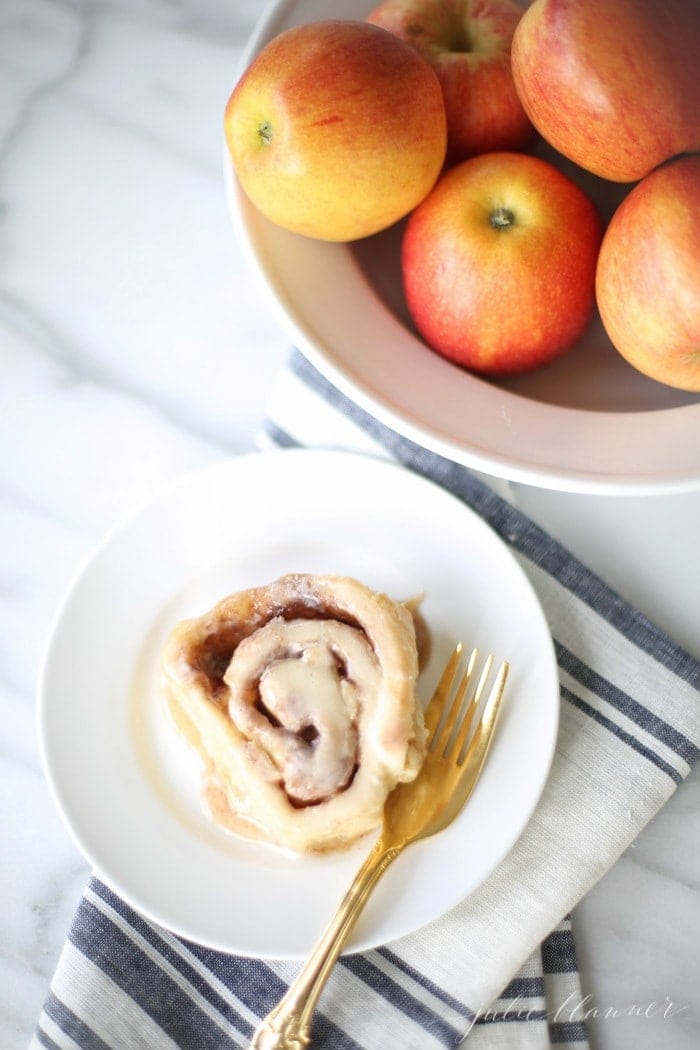 an apple cinnamon roll served on a white plate with a fork