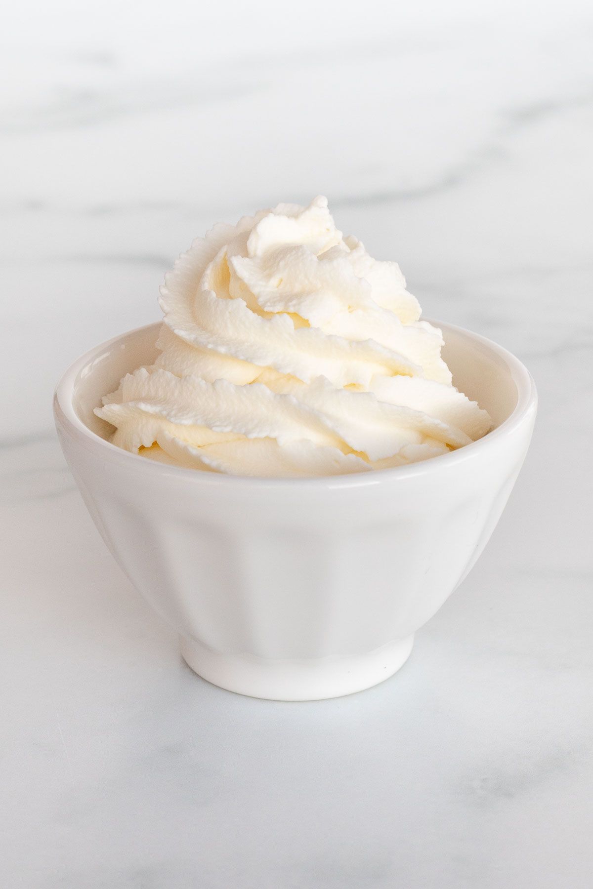 A white bowl full of whipped mascarpone cream on a marble surface.