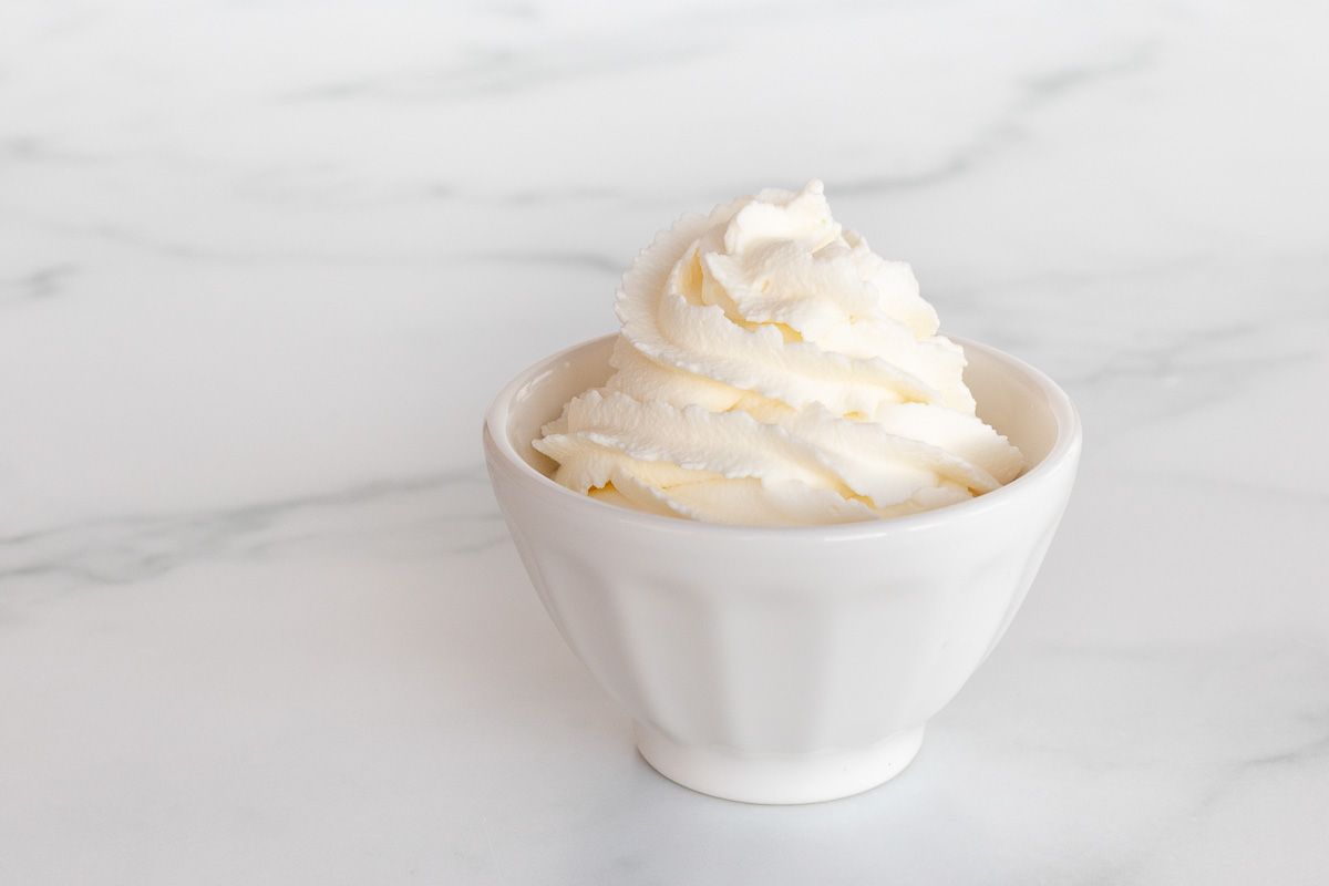 A white bowl full of whipped mascarpone cream on a marble surface.