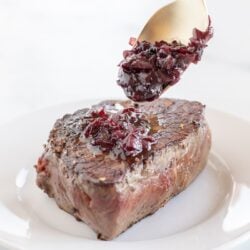 A steak on a white plate, with a gold spoon full of red wine jus being drizzled over it