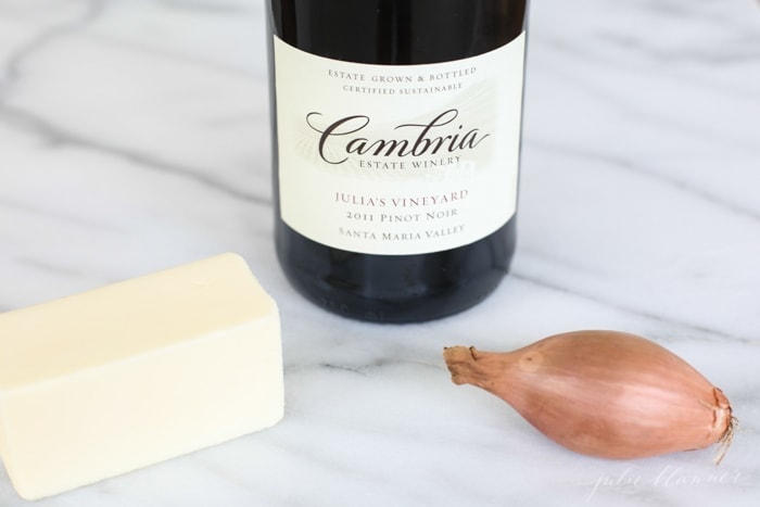 An incredible Red Wine Sauce for Steak that can be made in less than 20 minutes! Whether you call it red wine jus or gravy, its such an elegant meal! bottle of red wine, stick of butter, shallot on marble countertop