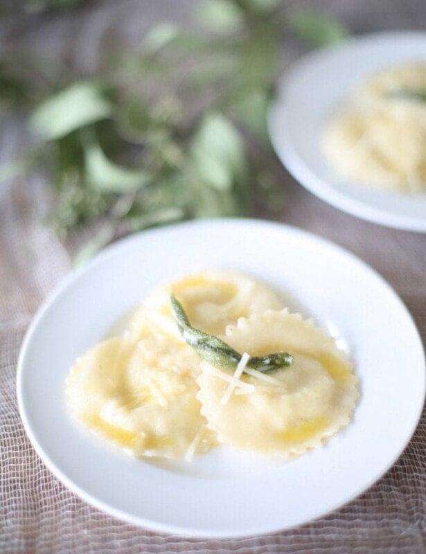 wonton ravioli in butter sage sauce on a white plate with sage leaves in background