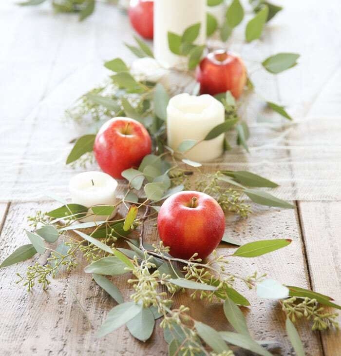 centerpiece on wood table with candles apples and eucalyptus
