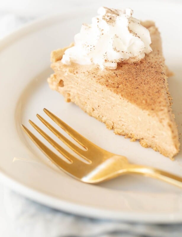 Pumpkin cheesecake topped with whipped cream on a white plate with a gold fork to the side.
