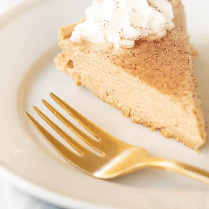 Pumpkin cheesecake topped with whipped cream on a white plate with a gold fork to the side.