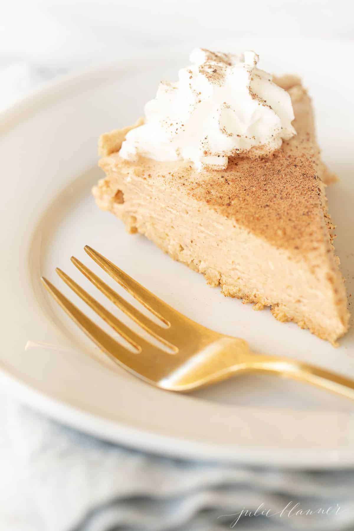 Pumpkin cheesecake topped with whipped cream on a white plate with a gold fork to the side. 