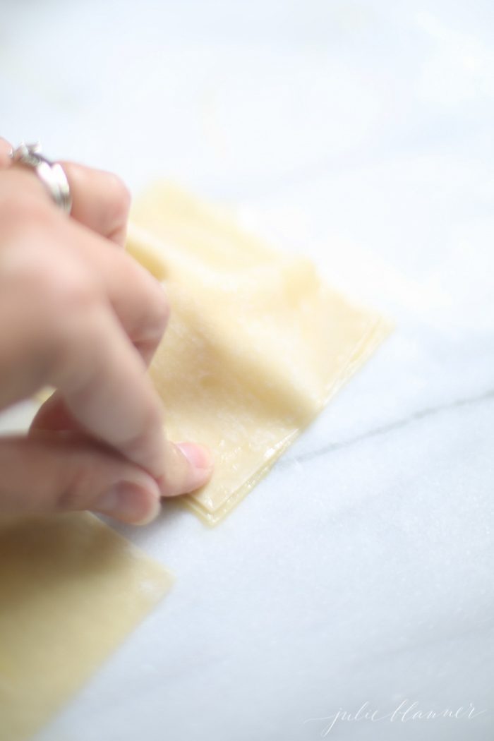 one hand sealing cheese filled wonton ravioli on marble countertop