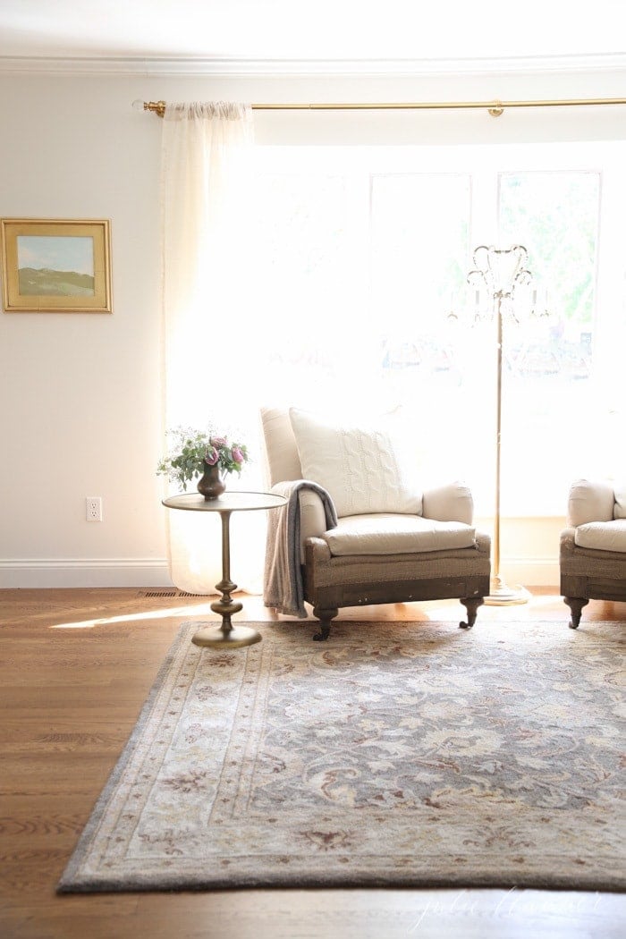 A living room with deconstructed Restoration Hardware linen chairs and a floral rug.