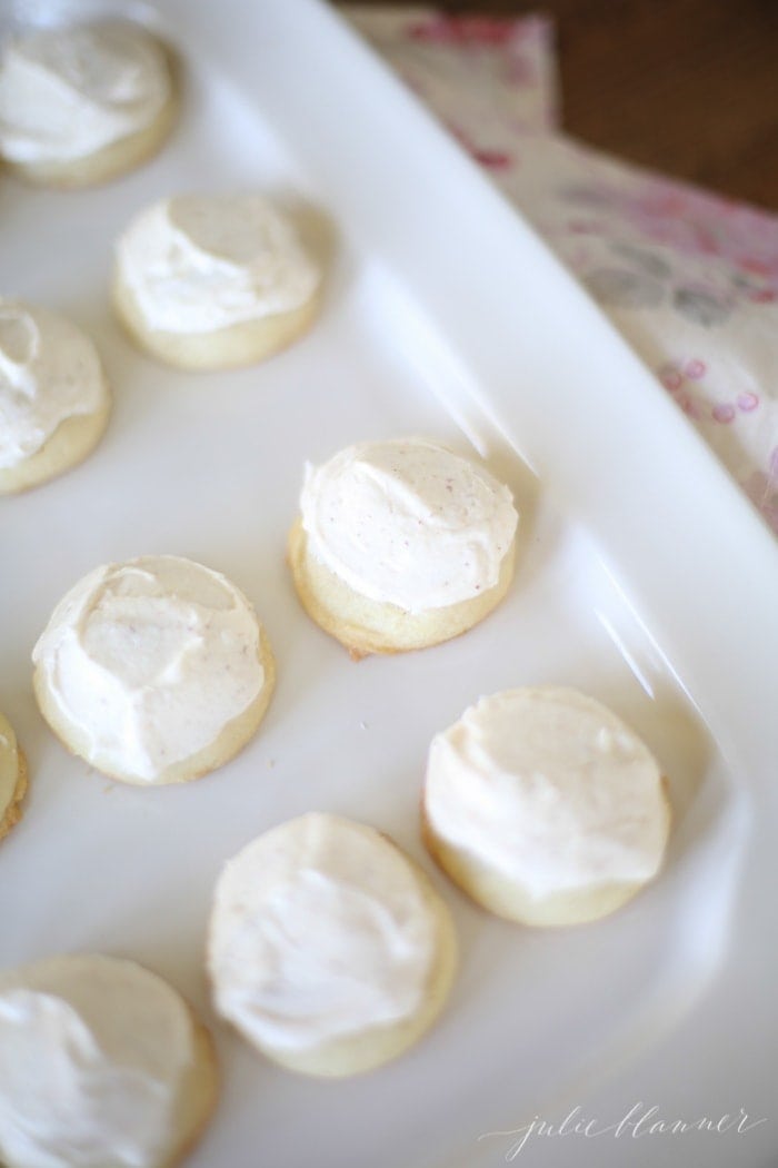 A white platter full of round browned butter sugar cookies topped with white frosting.