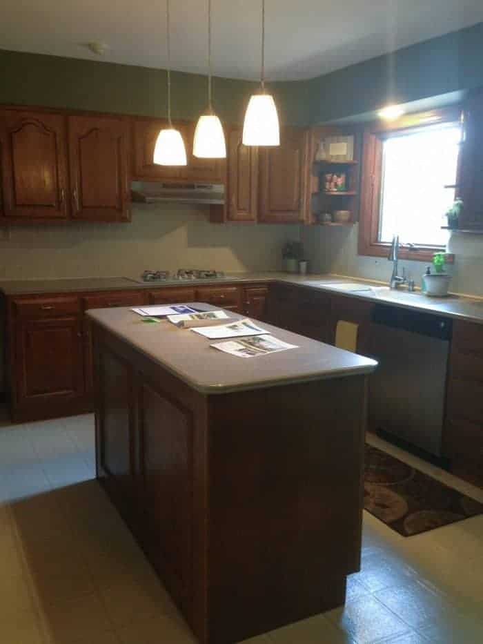 A dark and dated oak kitchen with outdated light fixtures.