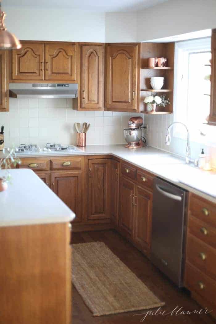 A modern kitchen with oak cabinets, fresh white paint, a jute rug, and copper accents.