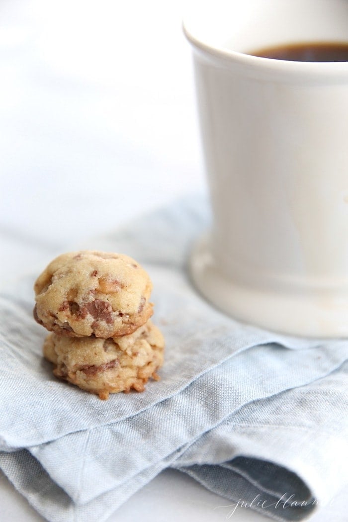 Toffee cookies stacked on a blue linen towel, white mug in background.