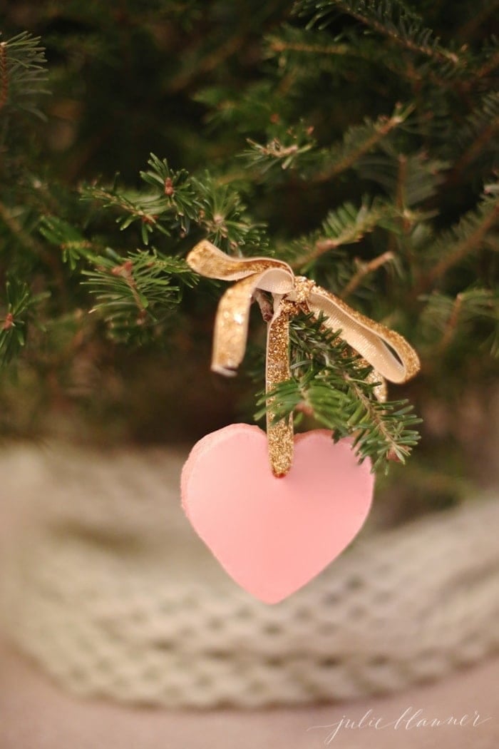 A pink heart color salt dough ornament hanging from gold ribbon on a Christmas tree.