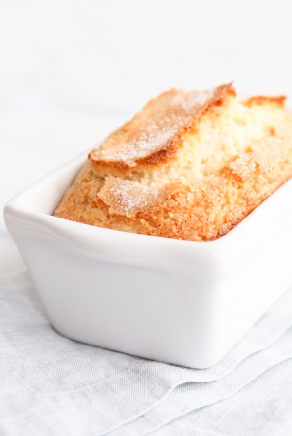 A golden brown sweet bread in a white rectangular baking dish placed on a light-colored cloth.
