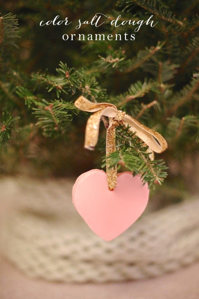 A color salt dough ornament shaped as a pink heart, hanging from a gold ribbon on a christmas tree.