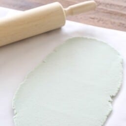 A color salt dough recipe rolled out as green dough on a sheet of parchment paper, wooden rolling pin to the side.