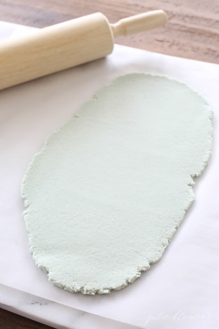 A color salt dough recipe rolled out as green dough on a sheet of parchment paper, wooden rolling pin to the side.