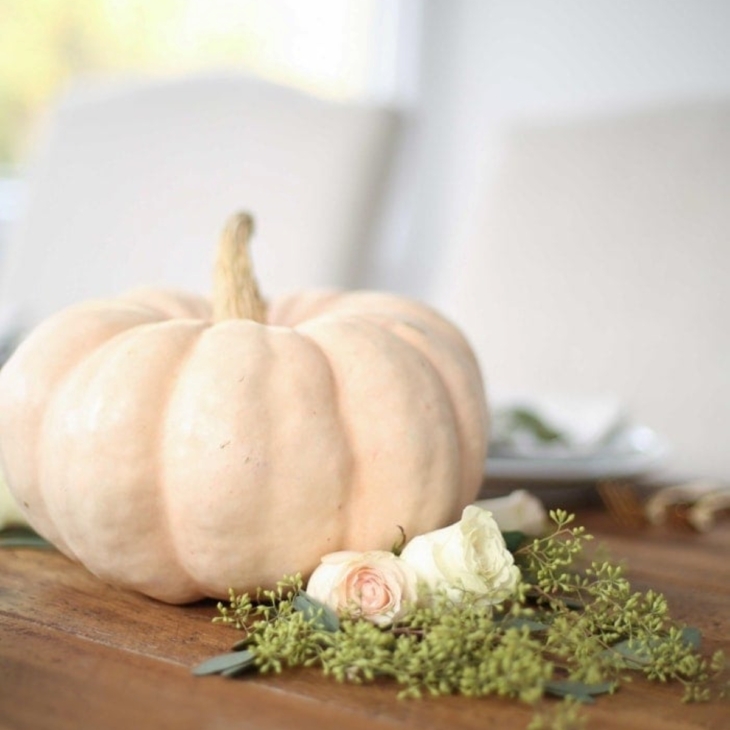 A Thanksgiving centerpiece set with a white pumpkin and fresh flowers below.