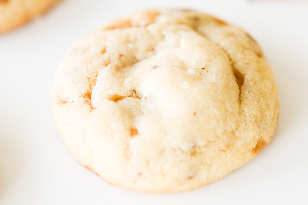 A close up of a toffee cookie on a white surface.