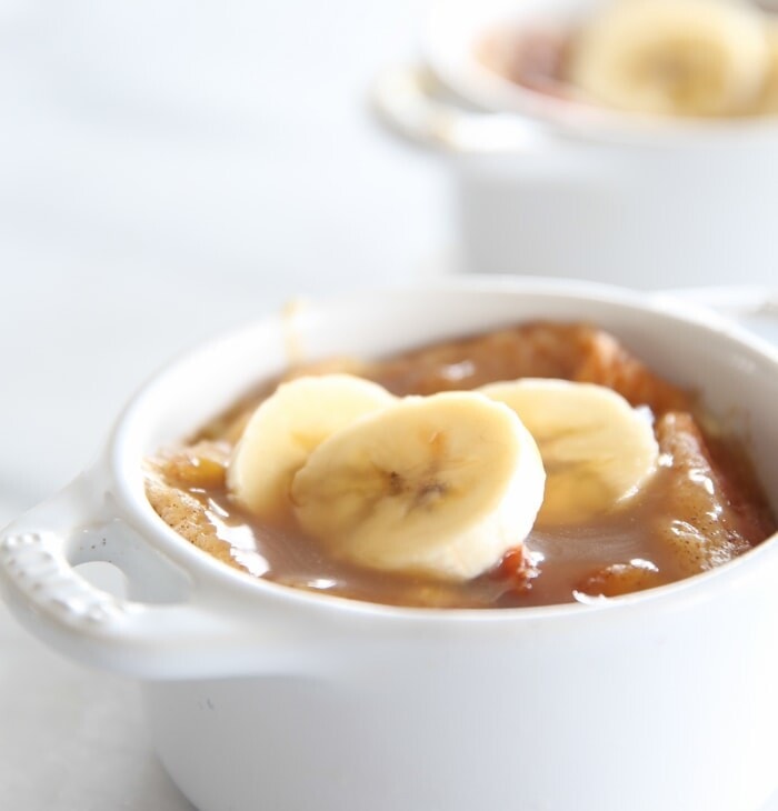 easy bread pudding topped with bourbon sauce and banana slices in two white individual baking dishes