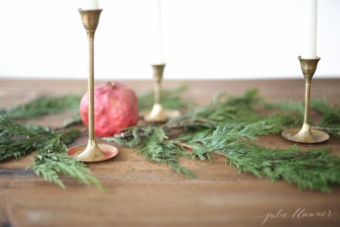 A stunning Christmas candle centerpiece featuring three brass candlesticks adorned with greenery and a pomegranate.