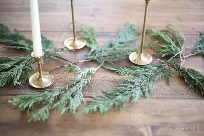 A festive Christmas candle centerpiece is created with three gold candle holders placed delicately on a wooden table.