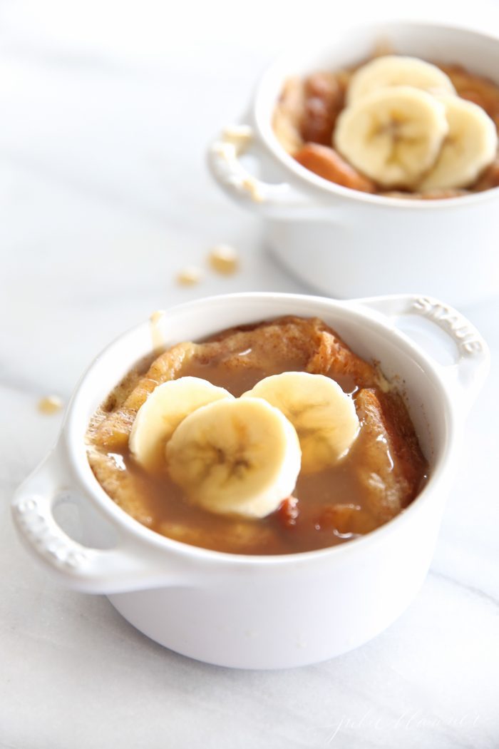 easy bread pudding topped with bourbon sauce and banana slices in two white individual baking dishes