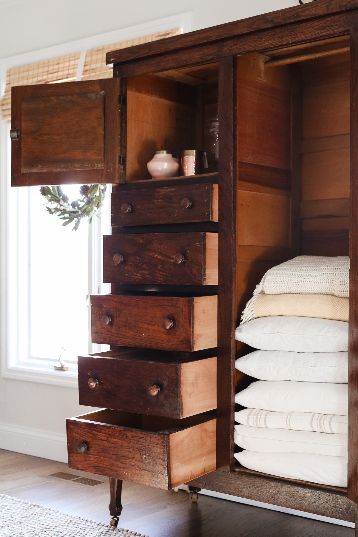 A dark wood linen cabinet in a family room space, with the drawers opened to reveal the interior storage.