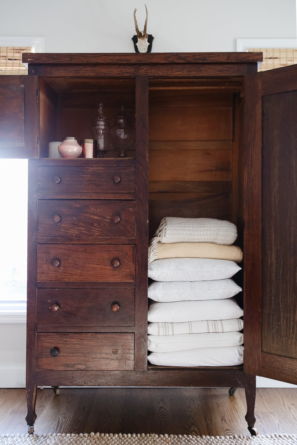 A dark wood linen cabinet in a family room space, with the door opened to reveal the interior storage.