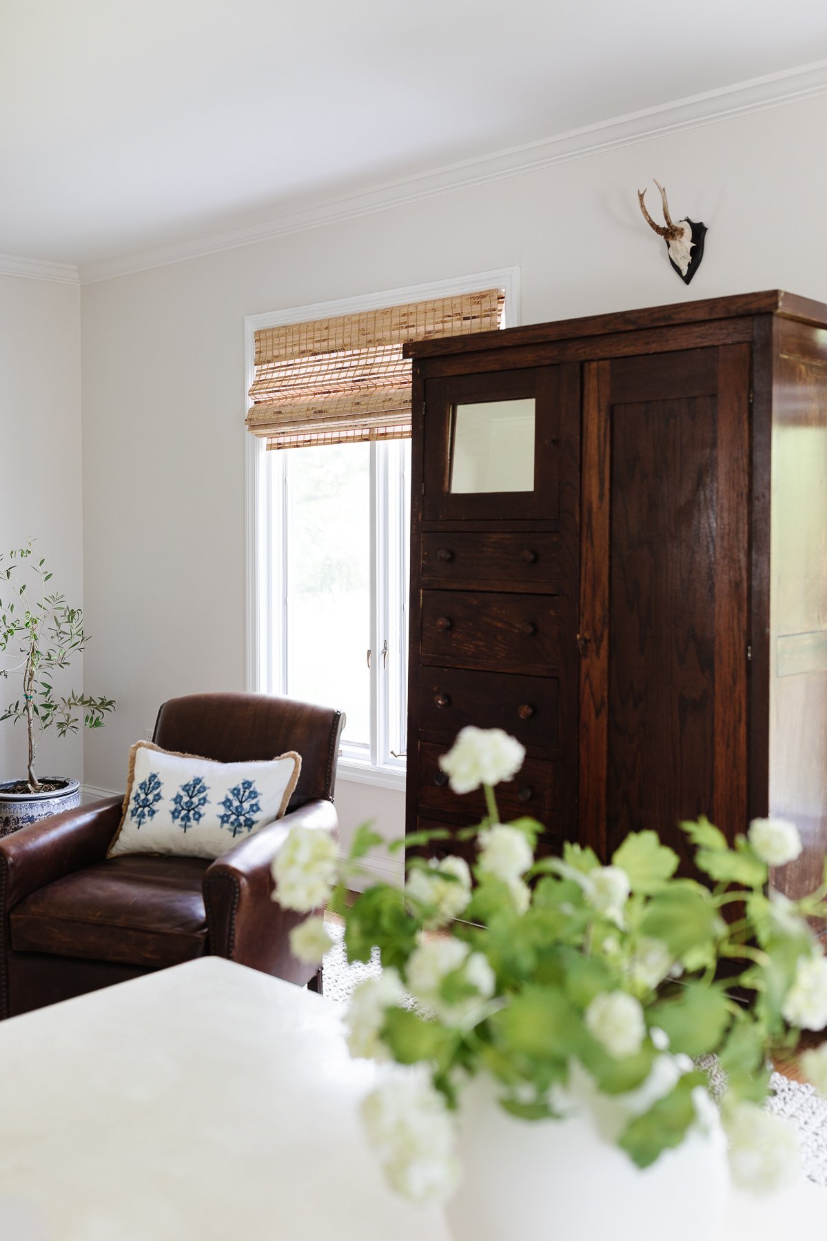 A white living room with a leather chair and a dark wood linen cabinet.