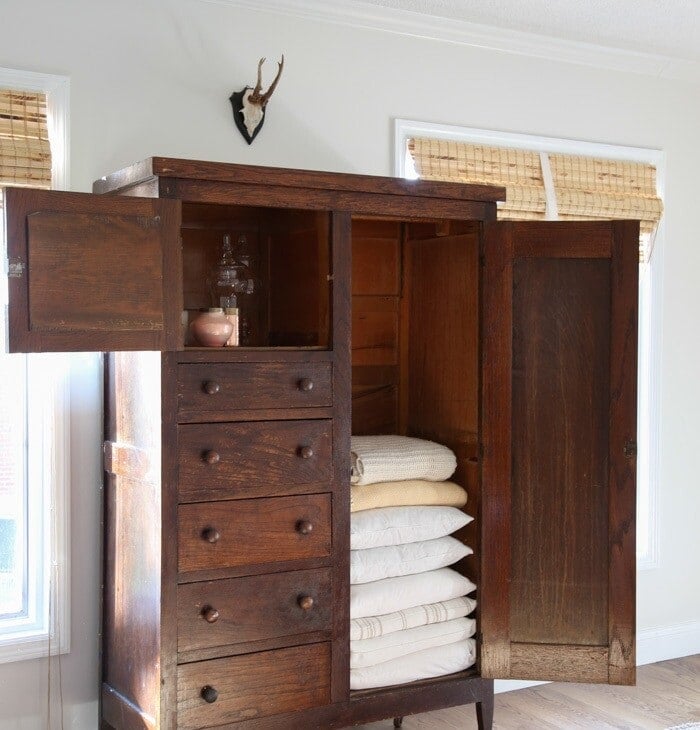 A white living room with a dark wood cabinet filled with linen organization