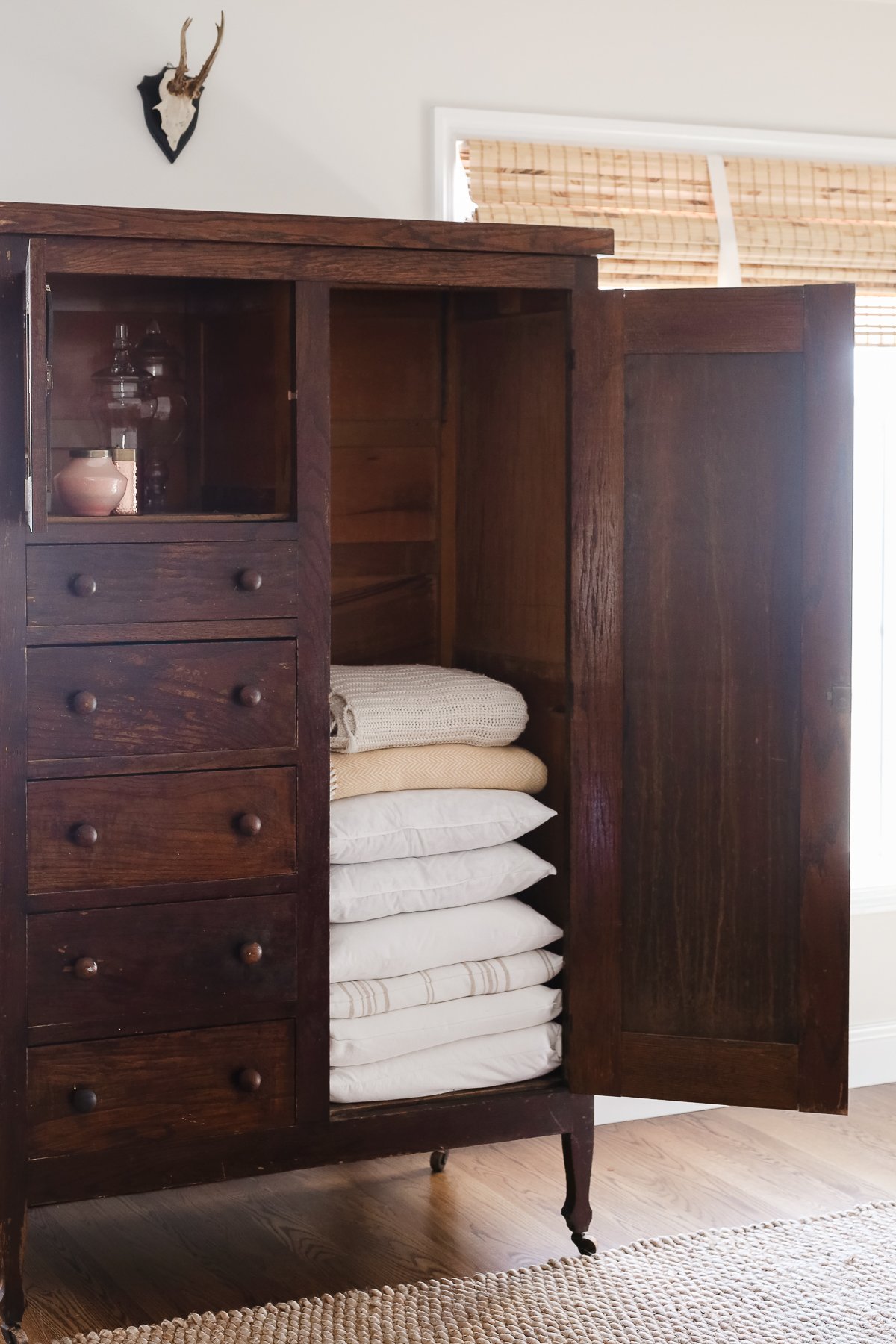 A dark wood linen cabinet in a family room space, with the door opened to reveal the interior storage.