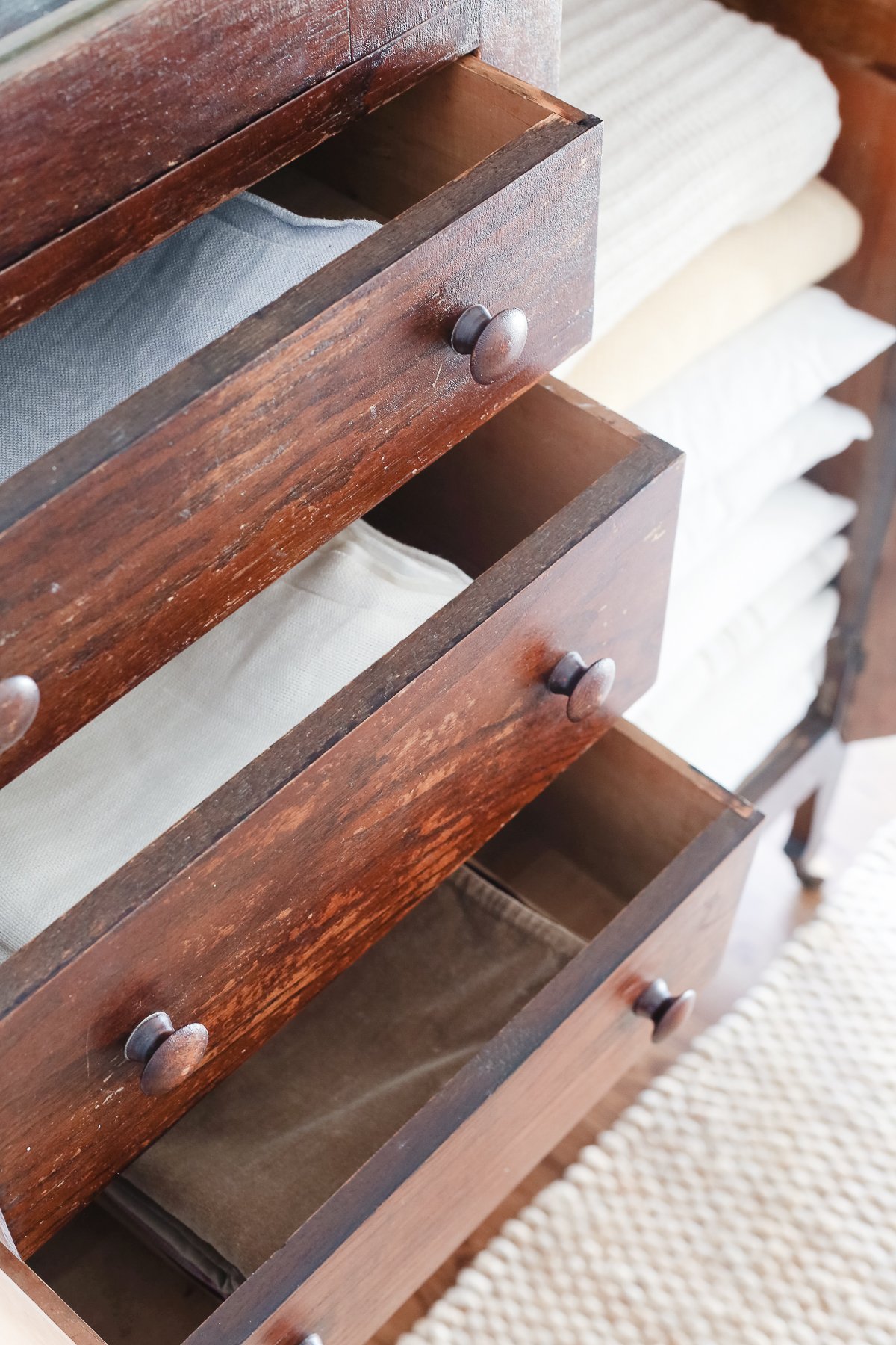 A dark wood linen cabinet in a family room space, with the drawers opened to reveal the interior storage.