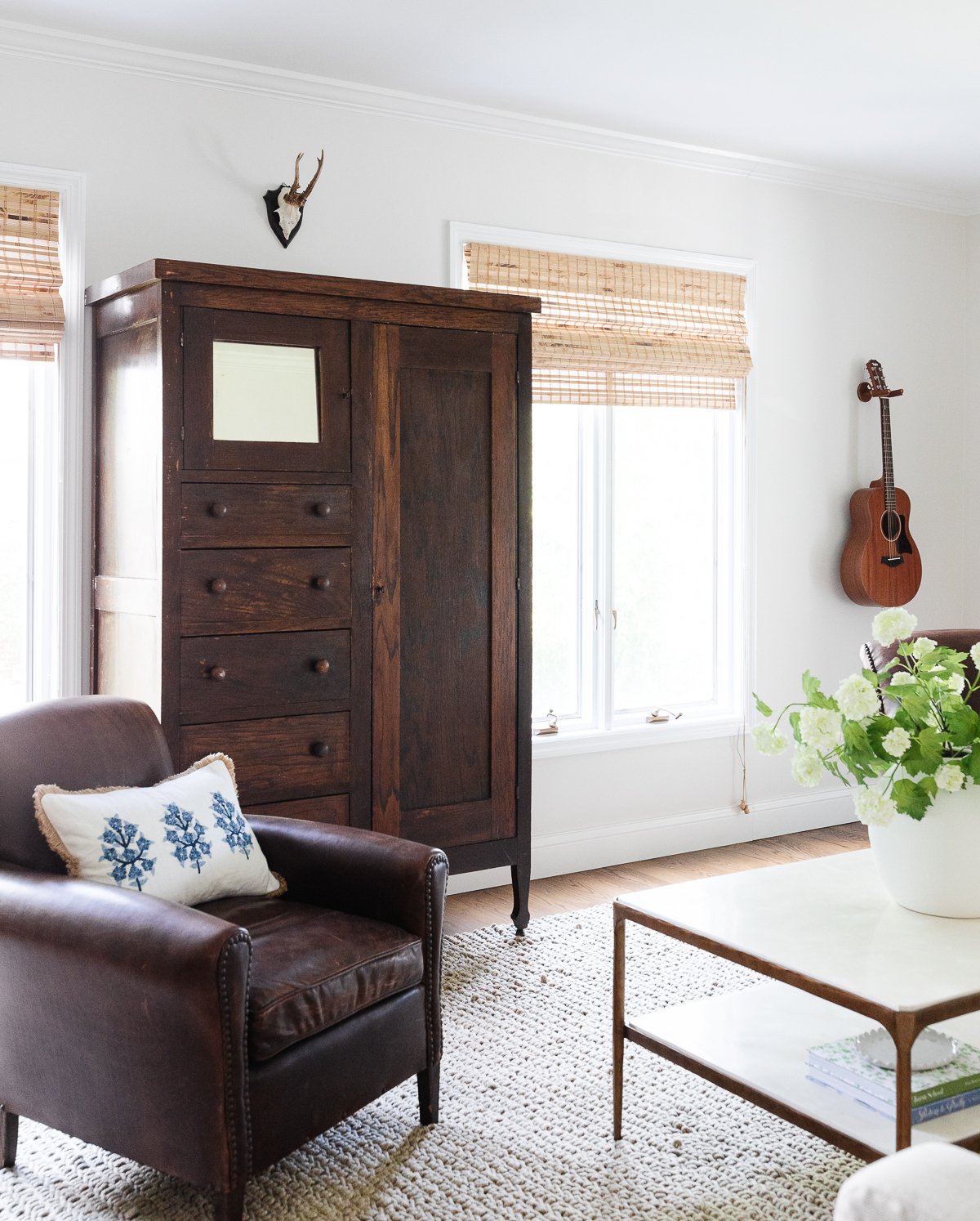 A white living room with a leather chair and a dark wood linen cabinet.