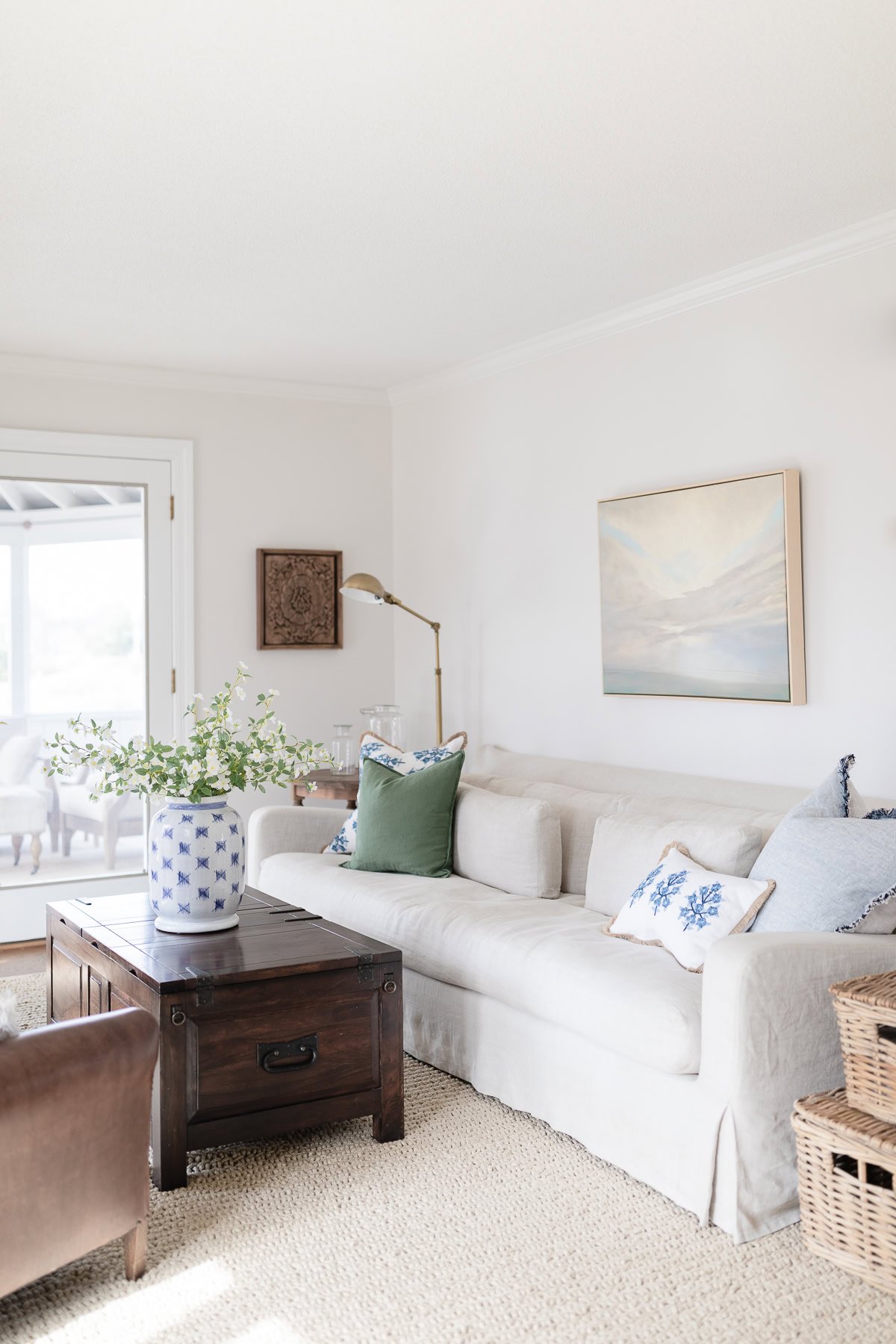 A bright living room with a white sofa, assorted pillows, a wooden coffee table with a blue and white vase, and neutral decor accents—perfect for those seeking tips on how to clean linen couch fabrics and keep spaces fresh.