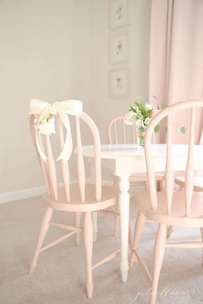 A small white table with soft pink wooden chairs in a child's bedroom.