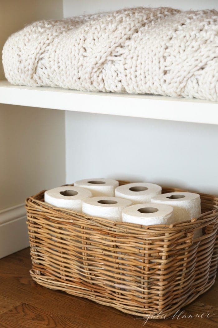 A linen closet organized with a wicker basket stacked with toilet paper rolls.